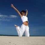 A woman jumping on the beach with her arms outstretched, seeking Sciatic Pain Relief and Sciatica Treatment.