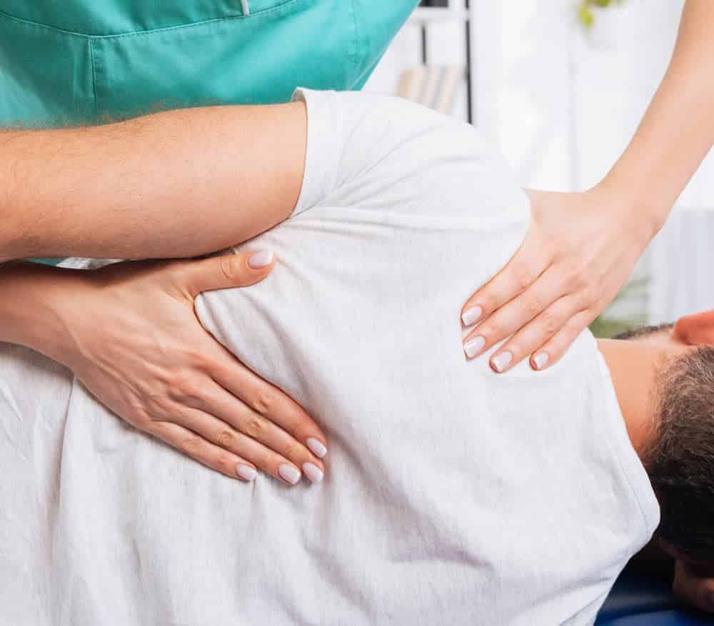 A man is having his back massaged by a physiotherapist.