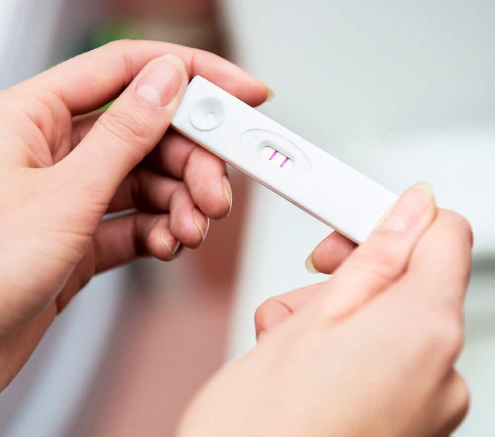 A woman's hand holding a thermometer in front of a toilet.