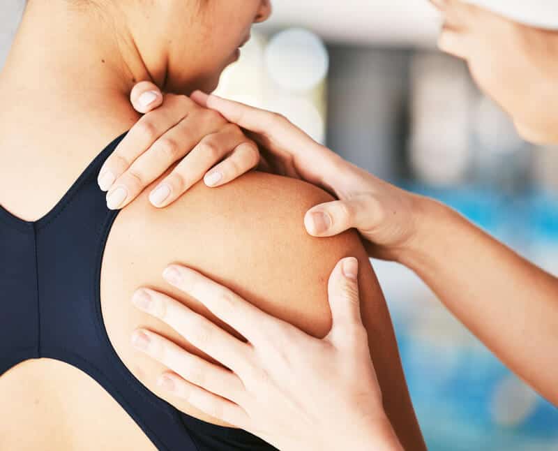 A woman is being helped by a physical therapist in a swimming pool.