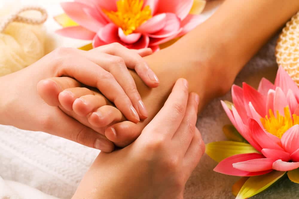 Hands Massaging A Foot Surrounded By Pink Flowers.