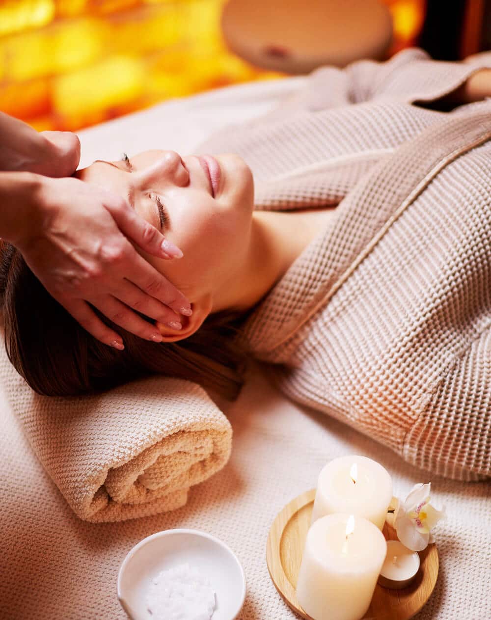 A Person Lies On A Massage Table Receiving A Head Massage, Surrounded By Candles And A Bowl Of Salts.