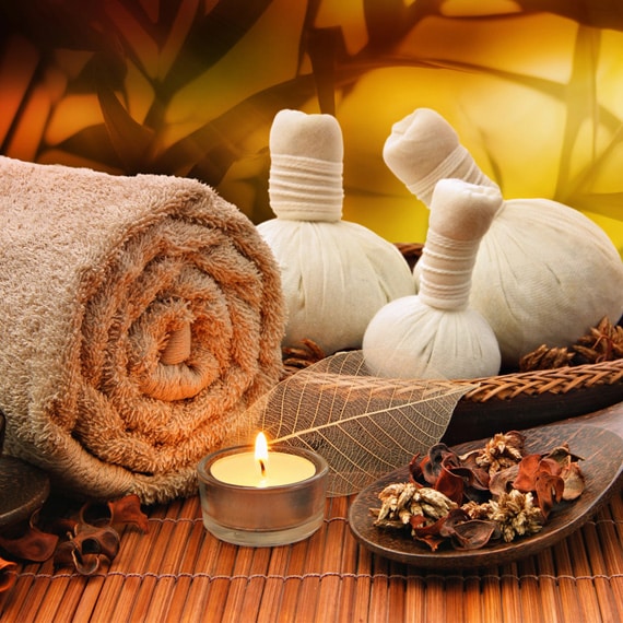 Spa Setting With Rolled Towel, Herbal Compress Balls, Lit Tea Candle, Dried Flowers, And Wooden Accents. Warm, Calming Ambiance.