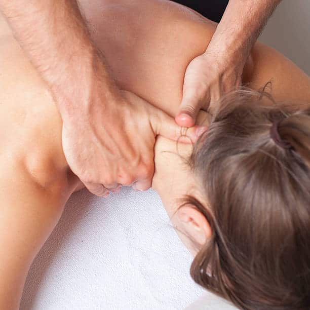 A Person Receives A Neck And Shoulder Massage While Lying Face Down On A White Towel.