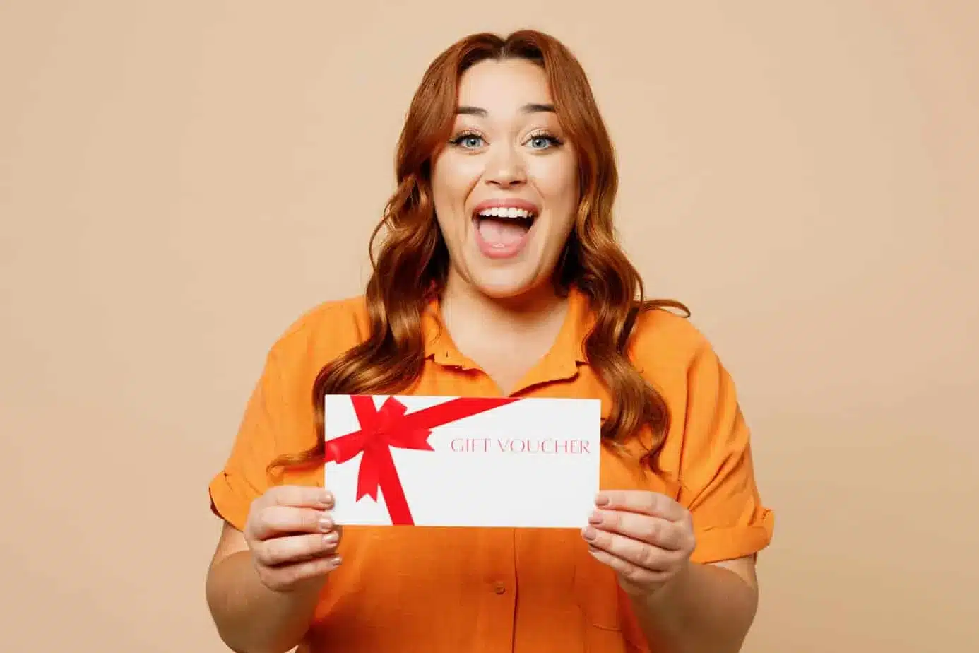 A woman holding up a gift card on a beige background. A woman holding up a gift certificate on a beige background.