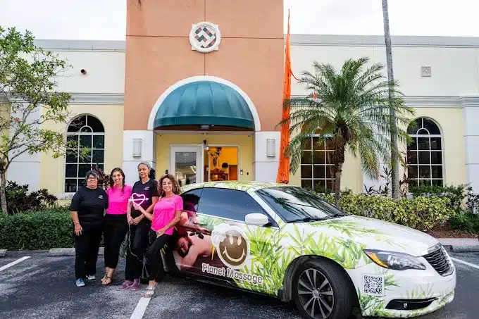 Four Women Stand Beside A Car With "planet Massage" Branding In Front Of A Beige Building With A Green Awning And Palm Tree.