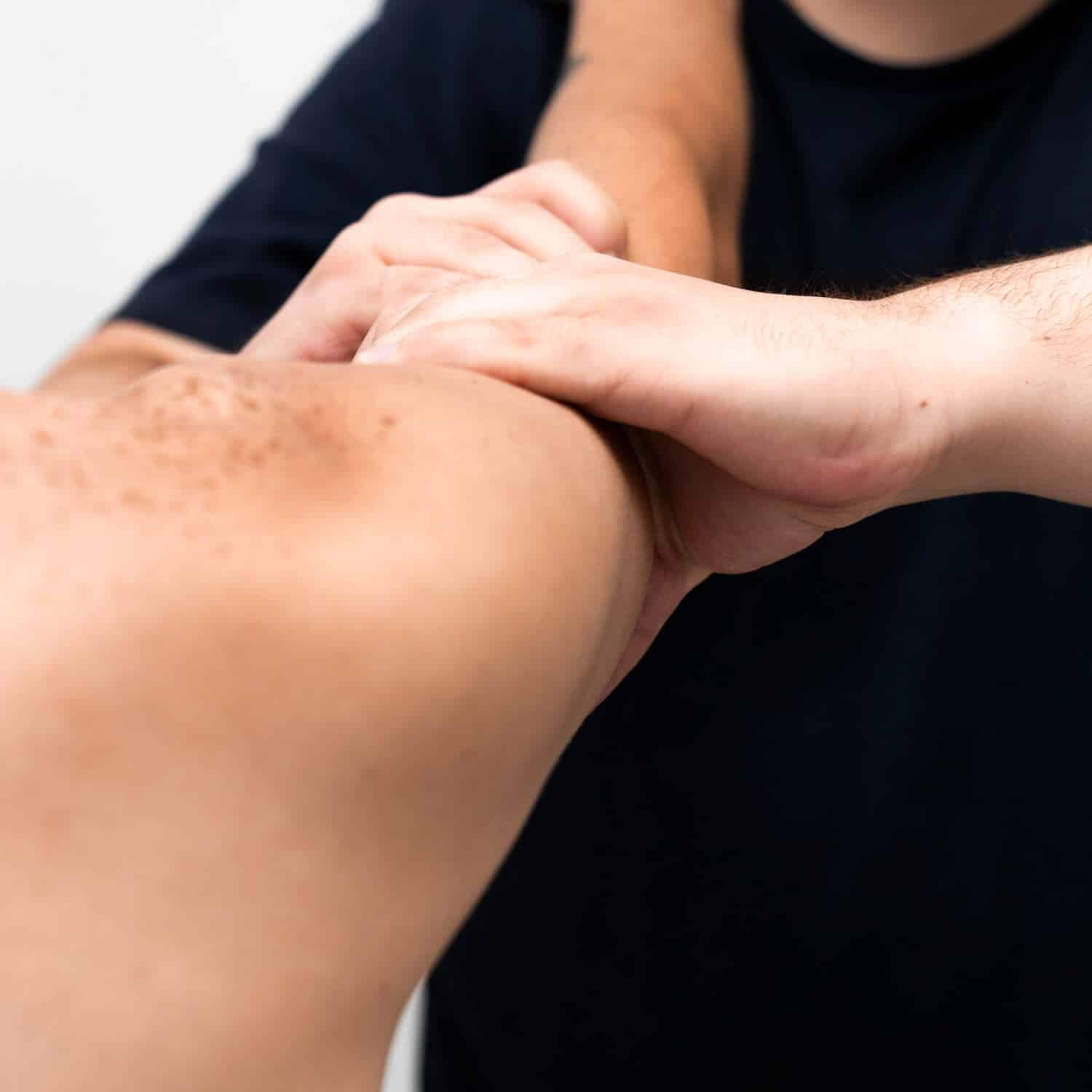 Close Up Of A Person Receiving A Physical Therapy Massage On Their Shoulder And Upper Arm By Another Person's Hands.