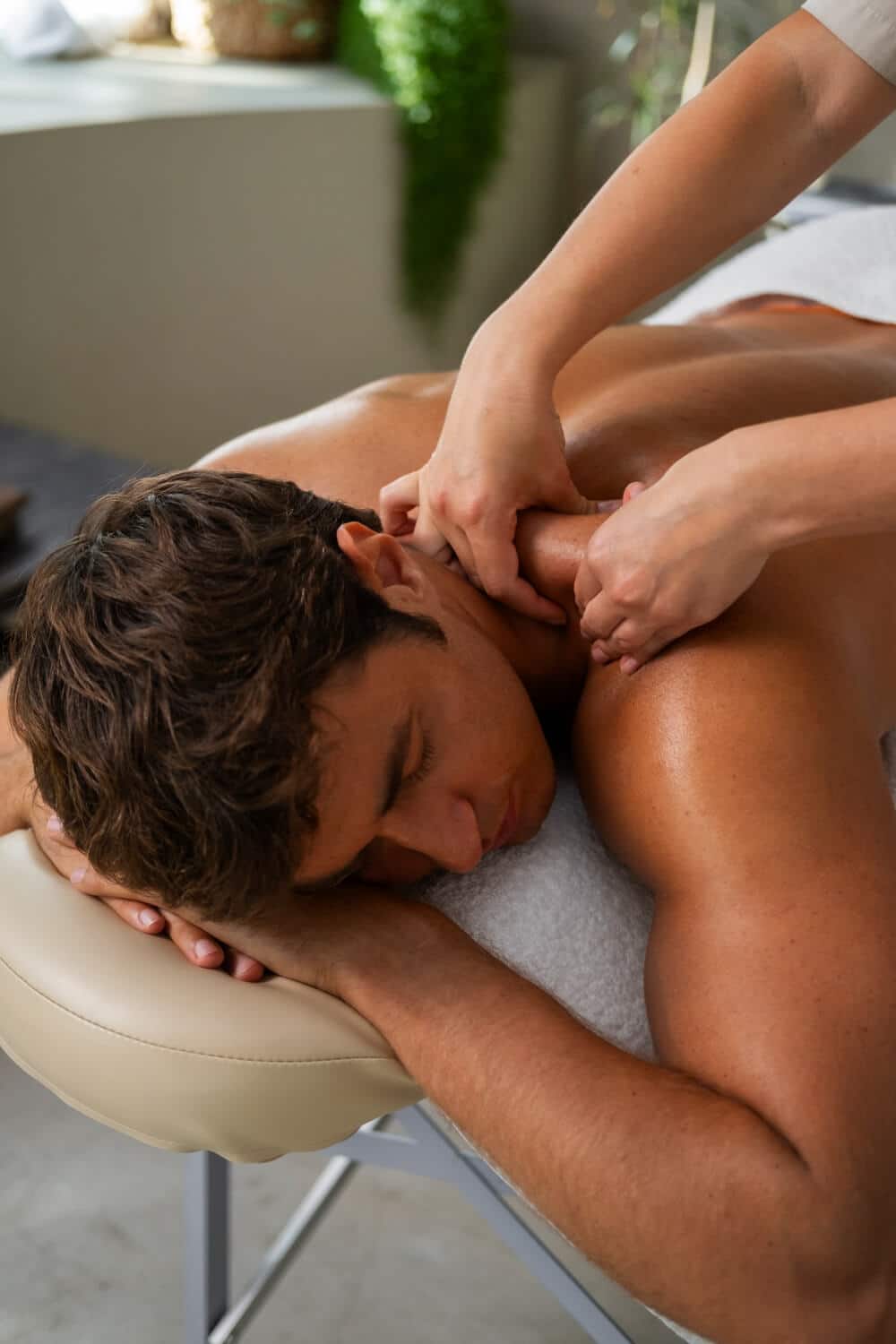 A Person Is Lying Face Down On A Massage Table While Receiving A Shoulder And Neck Massage From A Massage Therapist.