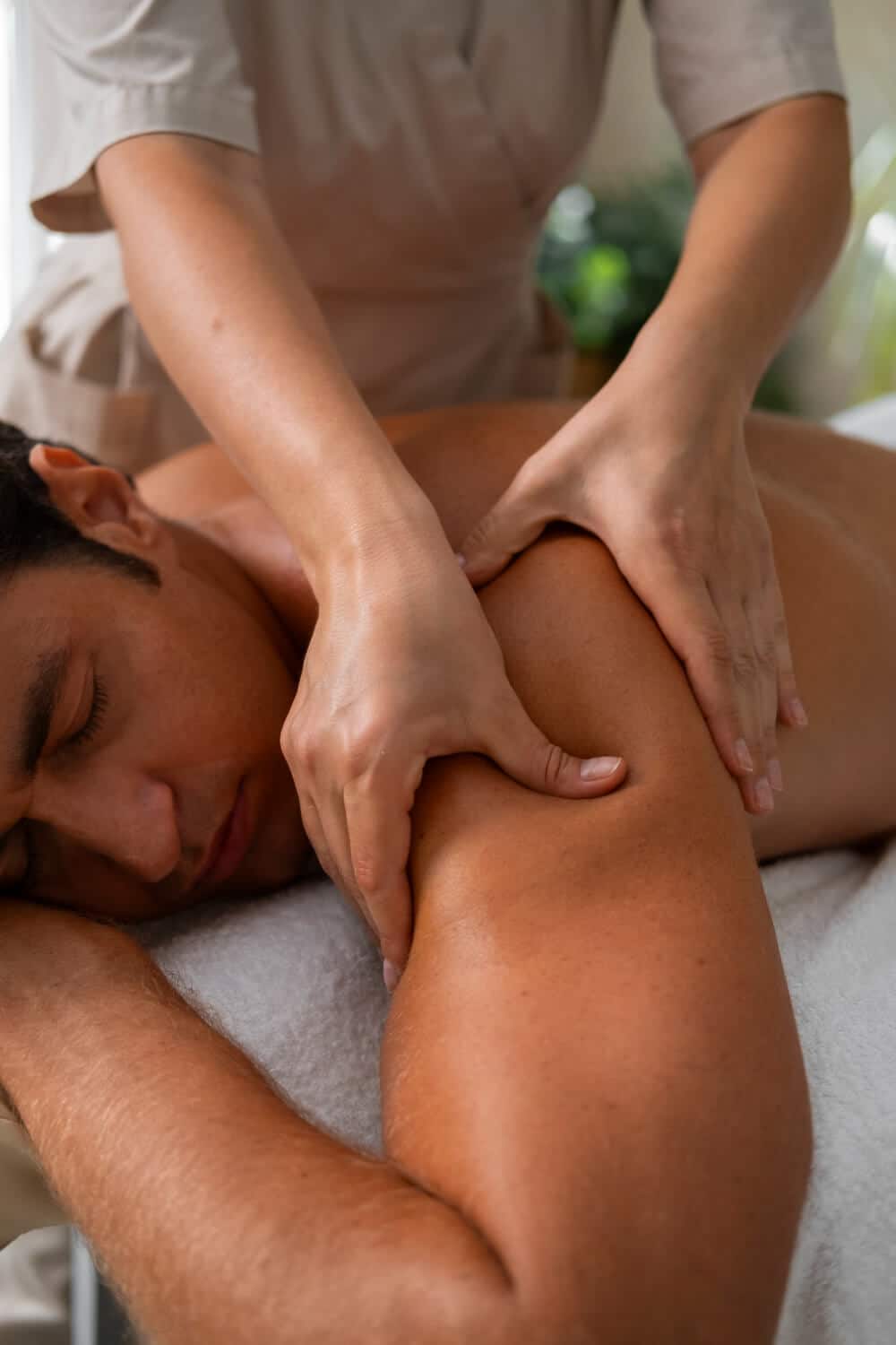 A Person Lying Face Down On A Massage Table Receives A Shoulder And Arm Massage From A Massage Therapist.